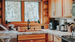 Una cocina con armarios de madera, un lavavajillas Bosch, una cafetera y una ventana con vistas a árboles.
