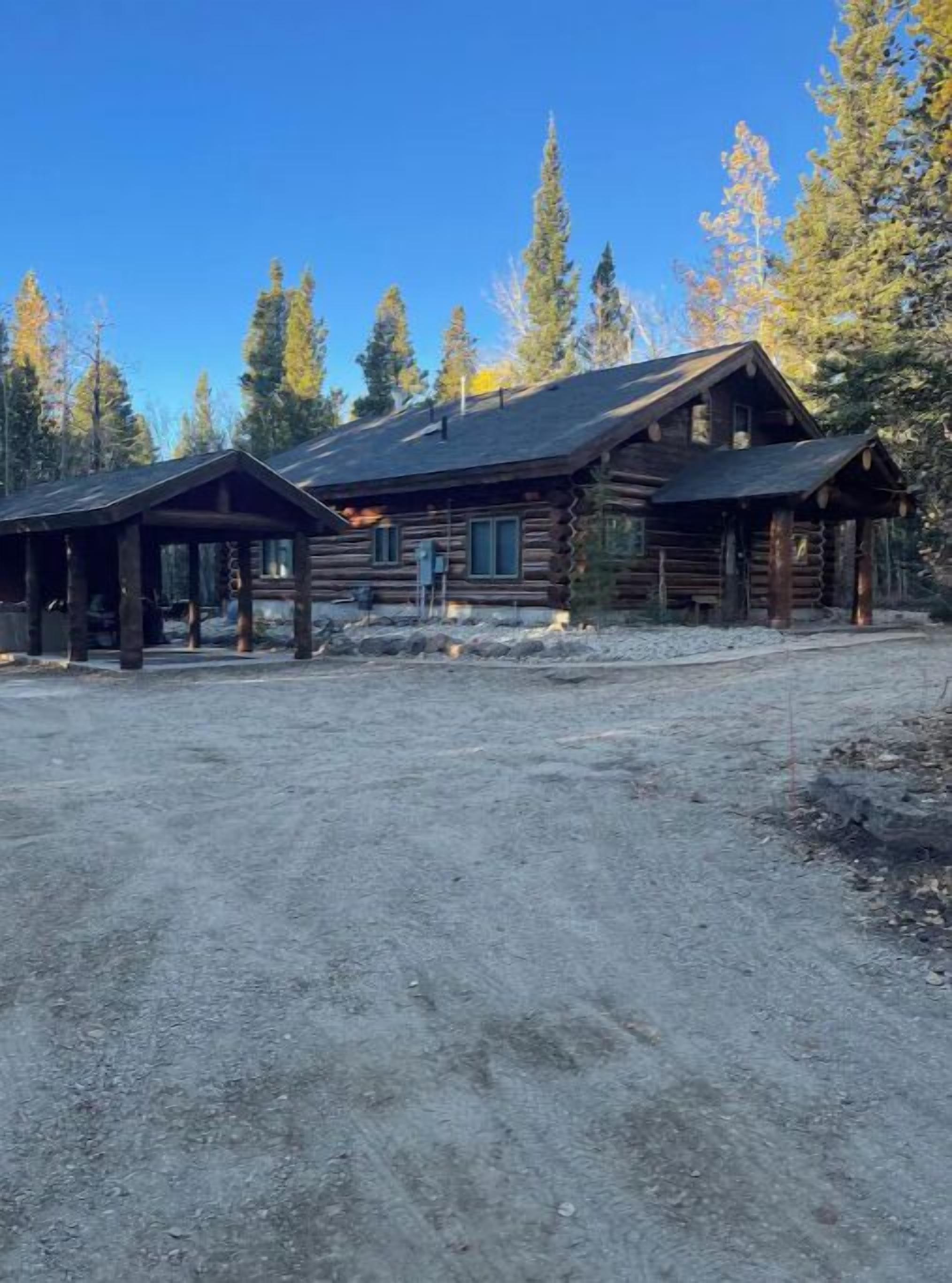 Une cabane en rondins avec un porche couvert et une allée en terre.