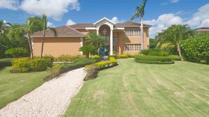 A two-story house with a beige exterior, a central entrance with a blue door, and a gravel pathway leading to the front. - Large Golf View Villa With Pool Jacuzzi and Staff (Punta Cana)
