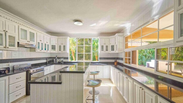 A spacious kitchen with white cabinetry, a large central island, and a view of greenery outside. - Large Golf View Villa With Pool Jacuzzi and Staff (Punta Cana)