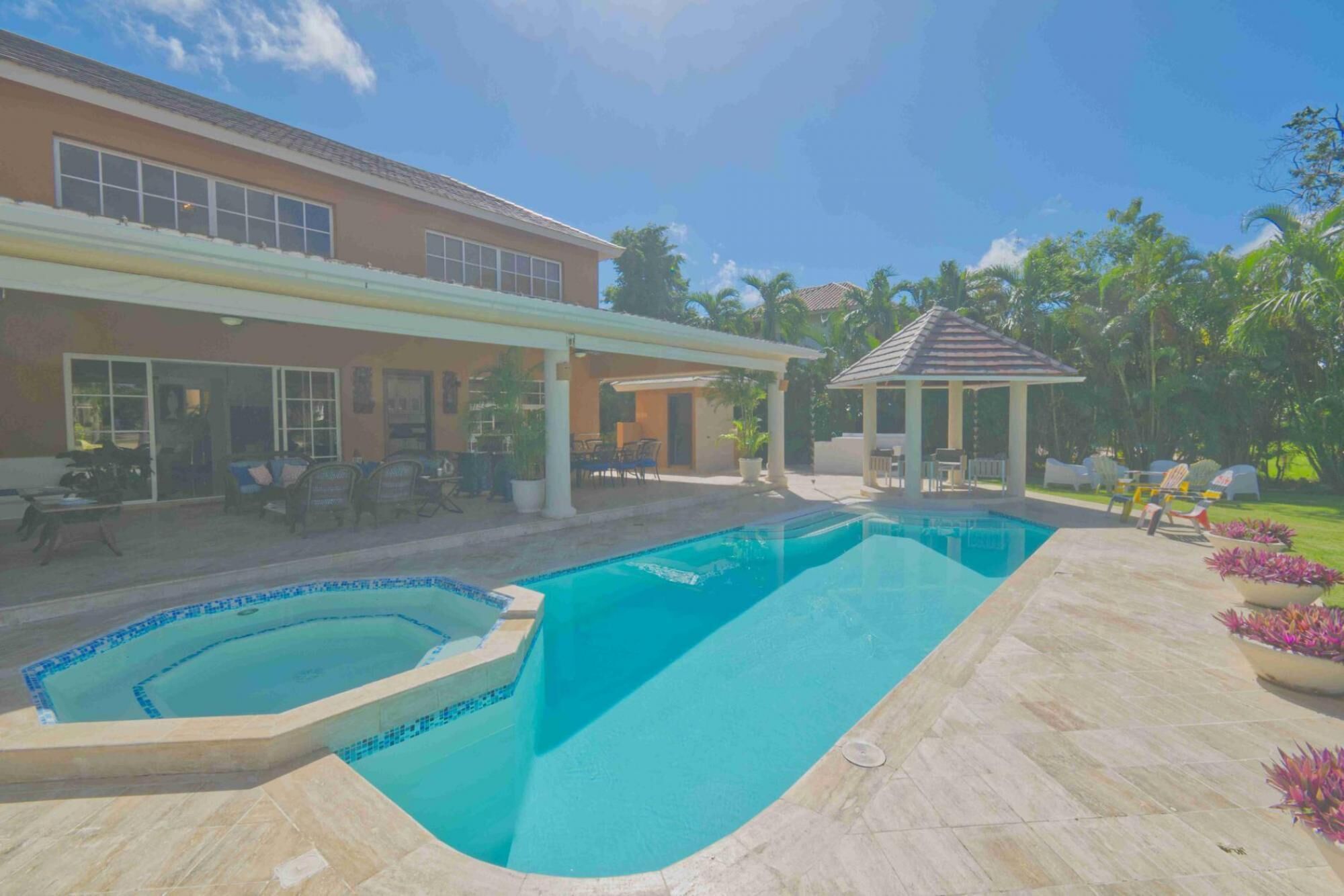 A swimming pool with a tiled deck, a covered patio area, and a gazebo.