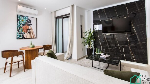 Een moderne woonkamer met een bank, een eettafel met stoelen, een accentmuur van zwart marmer en een groot raam.