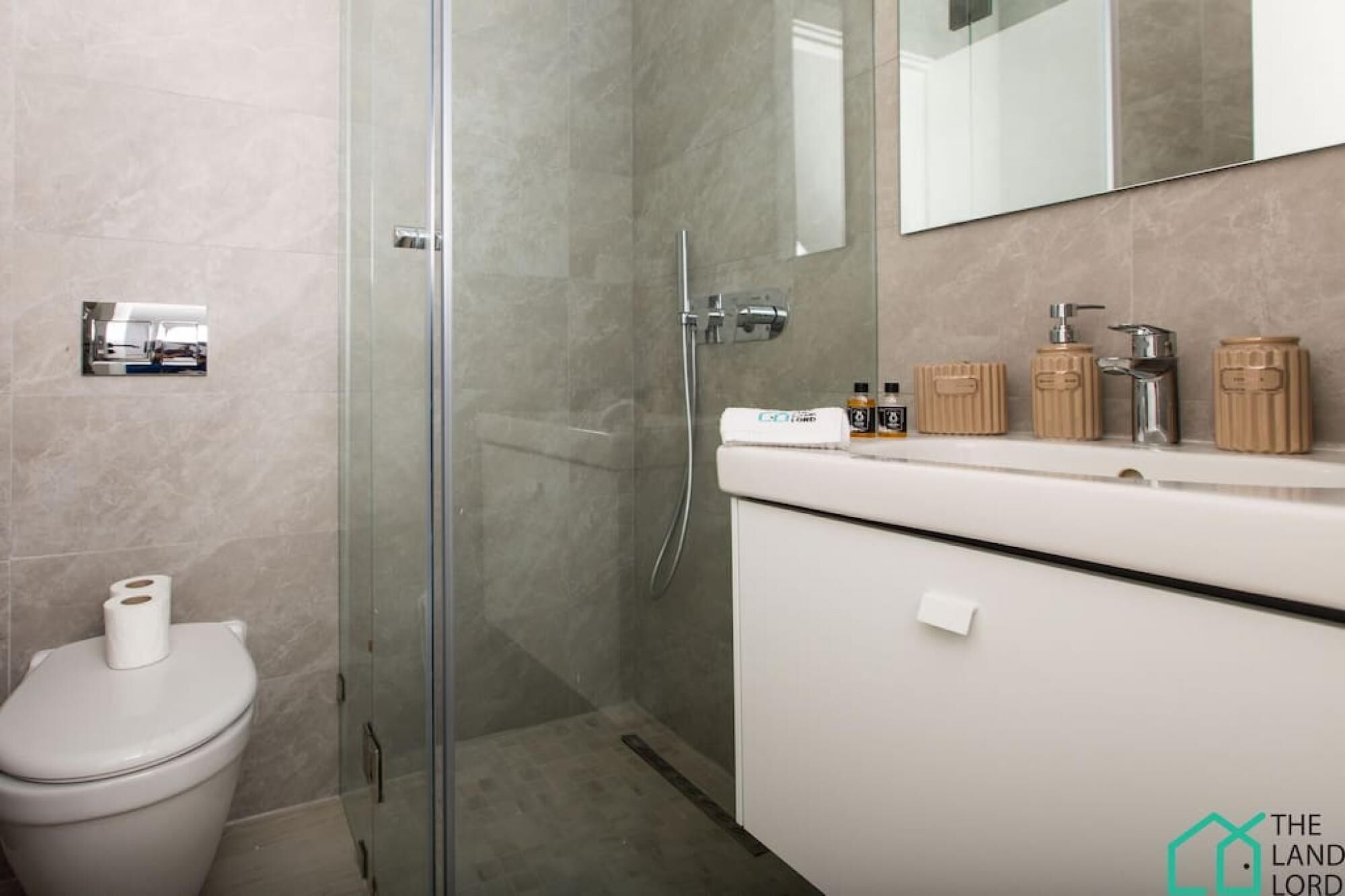 Un baño moderno con cabina de ducha de vidrio, inodoro y tocador con espejo.