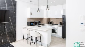 Een moderne keuken met witte kasten, een marmeren spatwand, een centraal eiland met barkrukken en hanglampen.