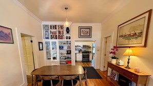 Zona pranzo con tavolo e sedie in legno, una libreria piena di libri e oggetti decorativi, una cucina sullo sfondo e un camino con una lampada.