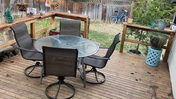 A wooden deck with a round glass table and four chairs, surrounded by potted plants and a bicycle.
