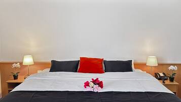 A neatly made bed with a red pillow, white and black bedding, and a floral arrangement. There are two bedside tables with lamps and a telephone.