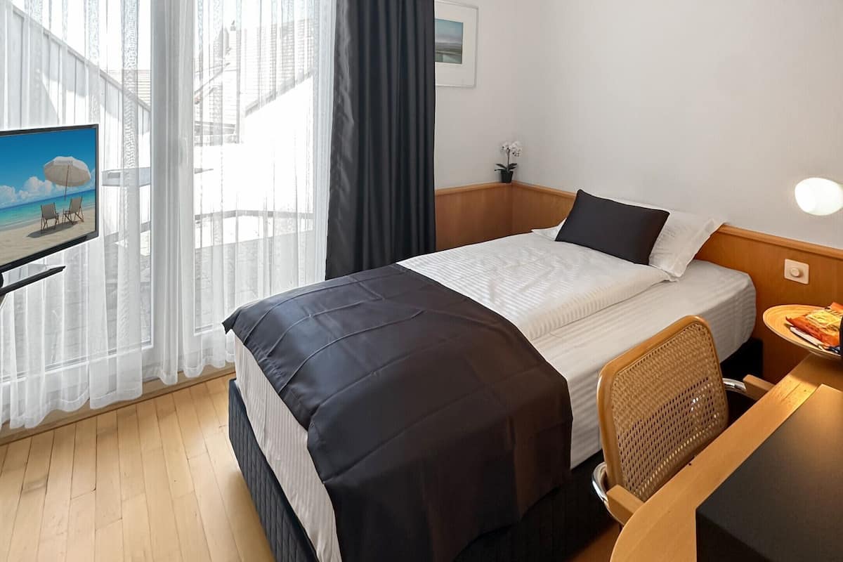 Ein Hotelzimmer mit einem Bett, einem Schreibtisch, einem Stuhl, einem Fernseher und einem Fenster mit Vorhängen.