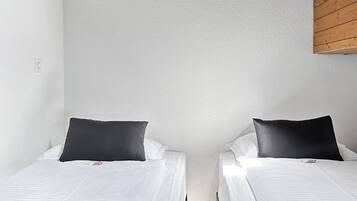 Ein Zimmer mit zwei Betten, weißer Bettwäsche, schwarzen Kissen und einer schrägen Holzbalkendecke.