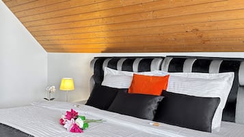 A modern bedroom with a sloped ceiling, a bed with striped bedding, and a bedside table with a lamp.