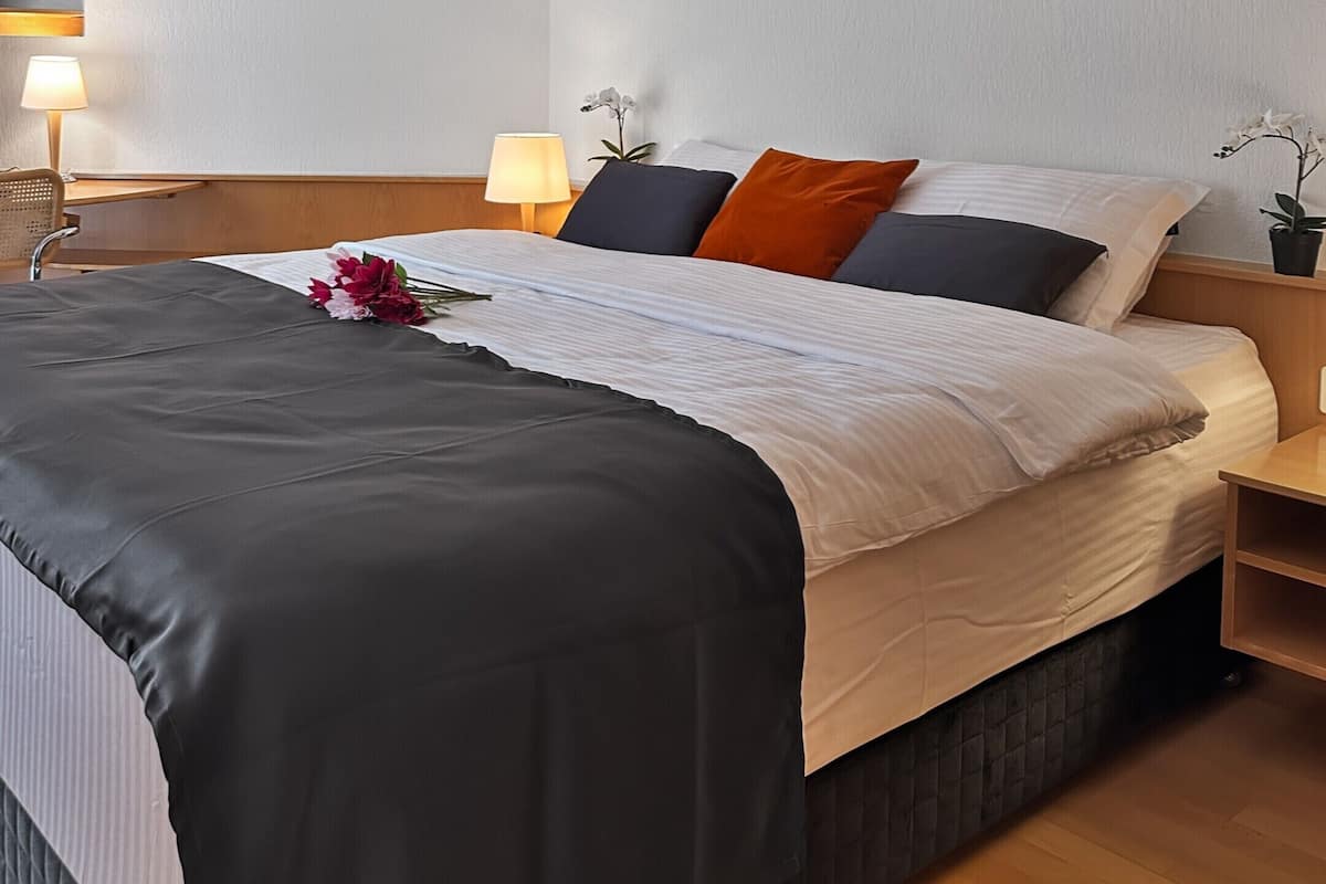 Ein Hotelzimmer mit einem Bett, Nachttischen, einer Lampe und einem Blumentopf.