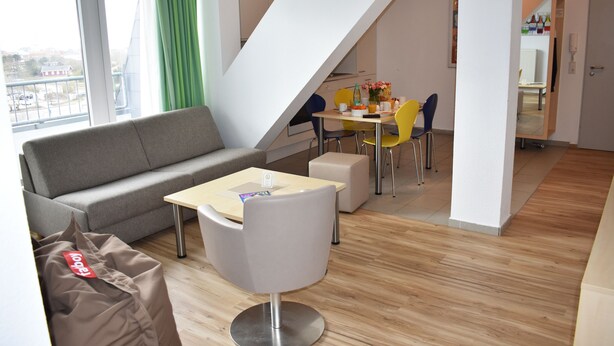 A modern living room with a sofa, a small table, and a dining area with chairs. - Posthus Apartment 305 with balcony, close to the beach and central (Borkum)