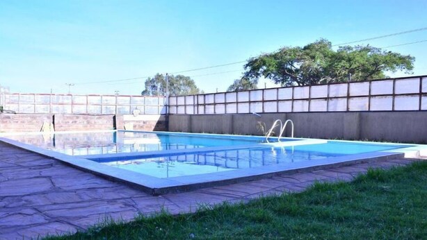 A rectangular swimming pool with a clear blue water surface, surrounded by a stone patio and a low concrete wall with a metal fence. - Essy's Furnished Homes Nakuru (Nakuru)