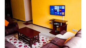 A living room with a sofa, a coffee table, and a flat-screen TV mounted on the wall. - Essy's Furnished Homes Nakuru (Nakuru)