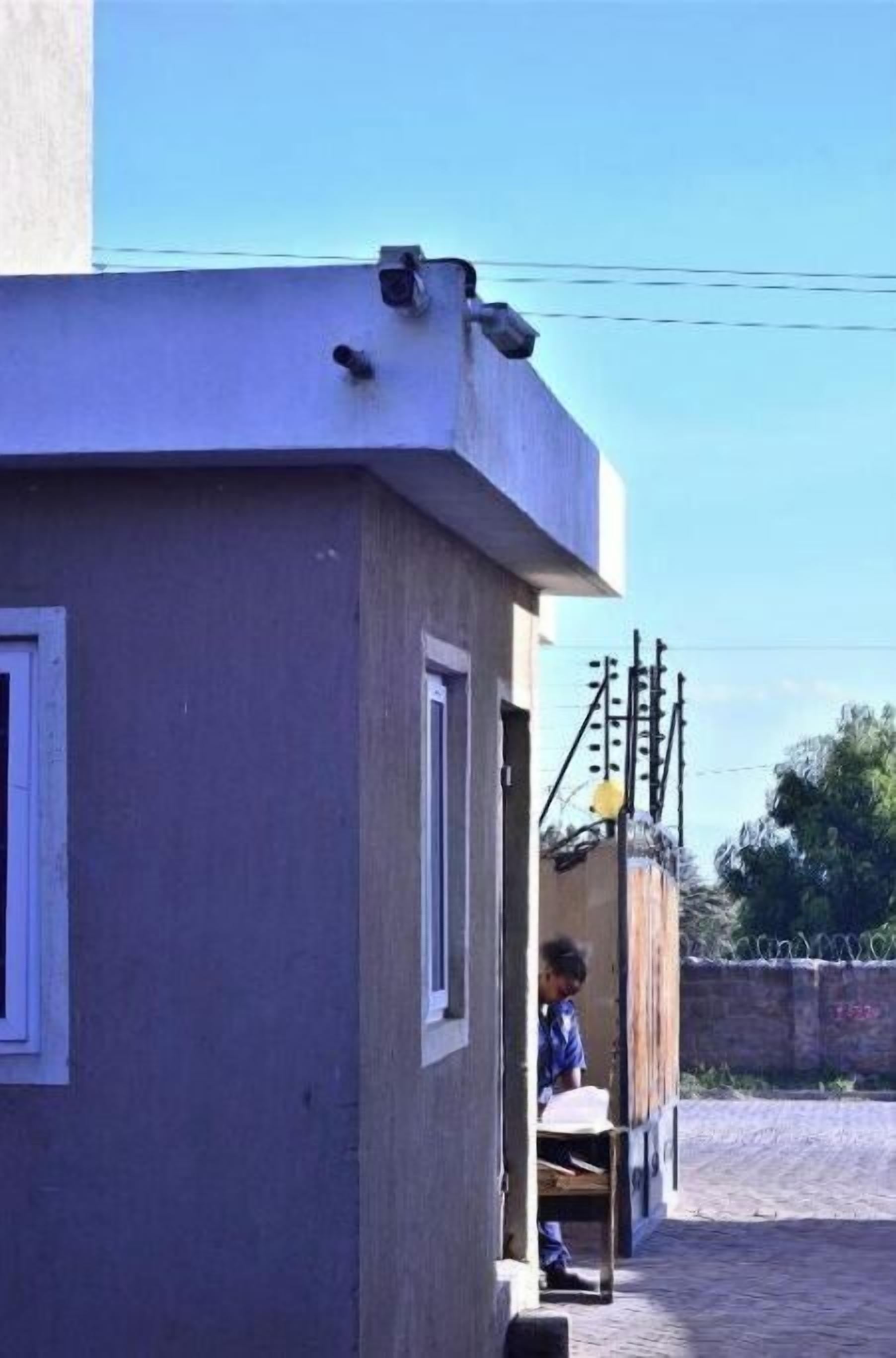A building with a flat roof, a window, and a door. There is a person sitting outside.