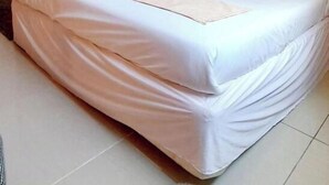A neatly made bed with white linens and a beige blanket, a wooden wardrobe, and a plain orange wall. - Essy's Furnished Homes Nakuru (Nakuru)