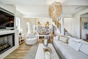 A spacious living room with a fireplace, white sofas, a coffee table, and a chandelier.