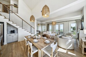 Amplia sala de estar con una mesa de comedor de madera dispuesta para cuatro personas, un sofá blanco y un ventanal con vistas al exterior.