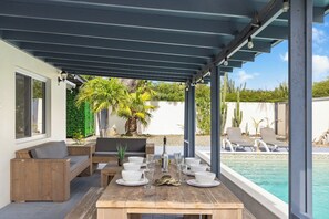 Eine Terrasse im Freien mit einem Holztisch, gedeckt für ein Essen, umgeben von Liegestühlen und einem Pool.