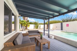Une terrasse extérieure avec une piscine, des meubles en bois et un espace abrité.