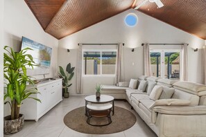 A modern living room with a sofa, a coffee table, and a TV. There are plants and a window with curtains. - Stylish 5BR Villa | Salina Sea La Vie | Pool (Noord)