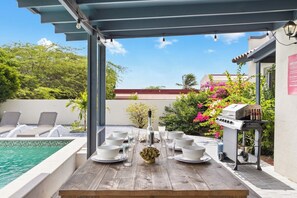 An outdoor dining area with a pool, lounge chairs, and a barbecue grill. - Stylish 5BR Villa | Salina Sea La Vie | Pool (Noord)