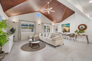 A spacious living area with a high ceiling, a large window, and a ceiling fan.