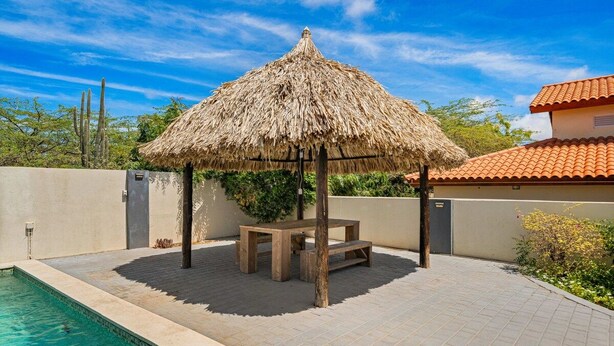 Un gazebo con tetto di paglia, una panchina, una piscina e un patio piastrellato.