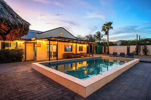 Zona junto a la piscina con piscina, sillas de descanso y un edificio con techo de paja.