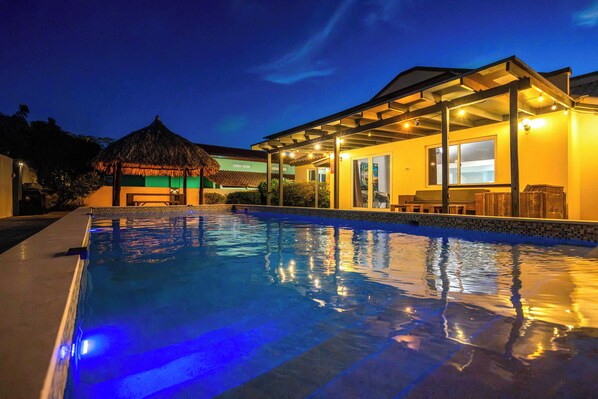 A swimming pool with a clear blue water surface, surrounded by a building with a covered patio area.