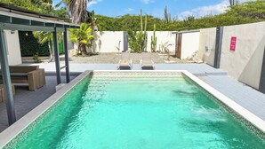 Una piscina rettangolare con bordo piastrellato, circondata da una terrazza con sedie a sdraio e una pergola.