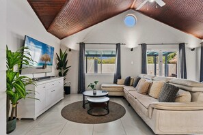 A modern living room with a sofa, a coffee table, and a TV on a white cabinet. There are plants and a painting on the wall. - Stylish 5BR Villa | Salina Sea La Vie | Pool (Noord)