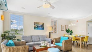 A living room with a sofa, coffee table, and wicker chairs. There is a dining area with a table and chairs. - Divi Aruba: 3BR Oasis w Free Parking near Beaches (Oranjestad)