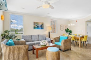 A living room with a sofa, coffee table, and wicker chairs. There is a dining area with a table and chairs. - Divi Aruba: 3BR Oasis w Free Parking near Beaches (Oranjestad)