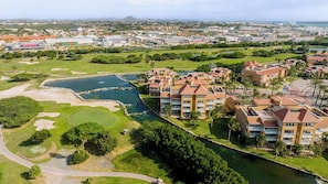 Un campo da golf con un elemento d'acqua, circondato da edifici alberghieri con diversi piani e balconi.