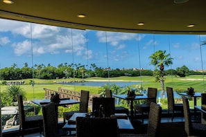 Ein Essbereich mit Tischen und Stühlen, mit Blick auf einen Golfplatz und ein Gewässer.