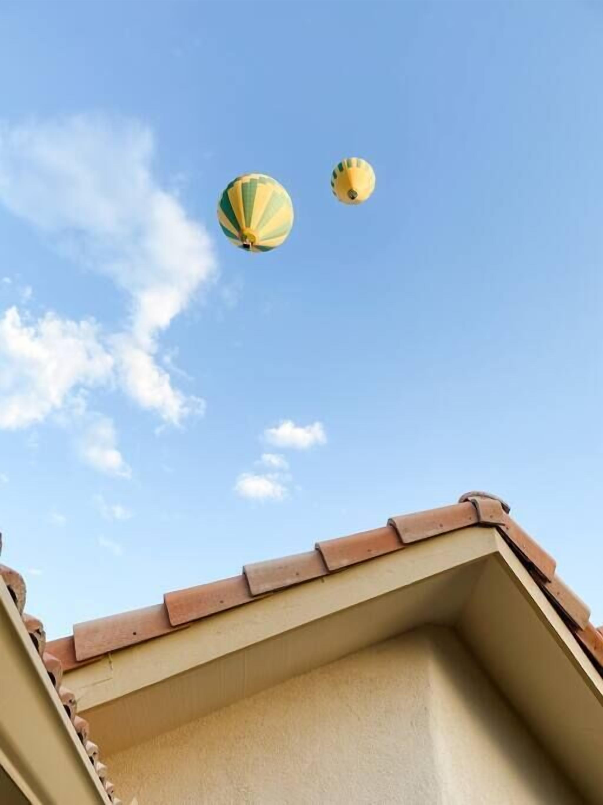 A building's roof with two hot air balloons in the sky.