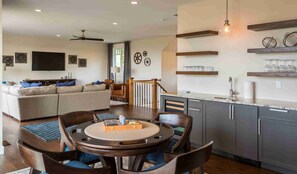 A modern living room with a sofa, a dining table with chairs, a kitchen area with a countertop and cabinets, and a ceiling fan. - Spacious Family Home Overlooking Little Traverse Bay (Harbor Springs)