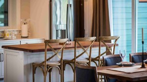 Une cuisine avec un îlot central en bois, quatre chaises en bois, un réfrigérateur en acier inoxydable et une fenêtre avec des rideaux.