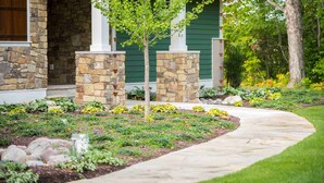 Une maison avec une façade en pierre, une porte verte et un jardin aménagé avec un chemin.