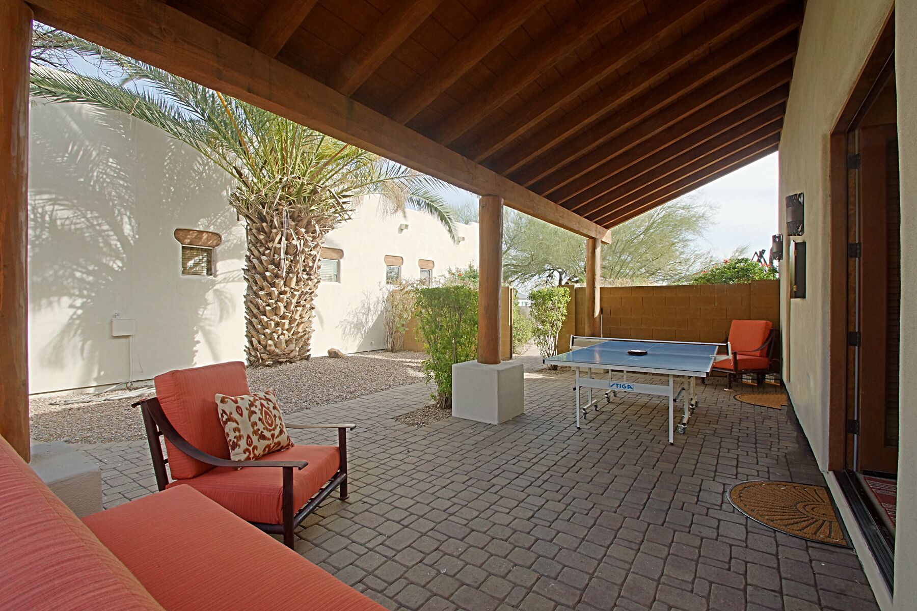 An outdoor patio with a ping pong table, a red sofa, and a palm tree.