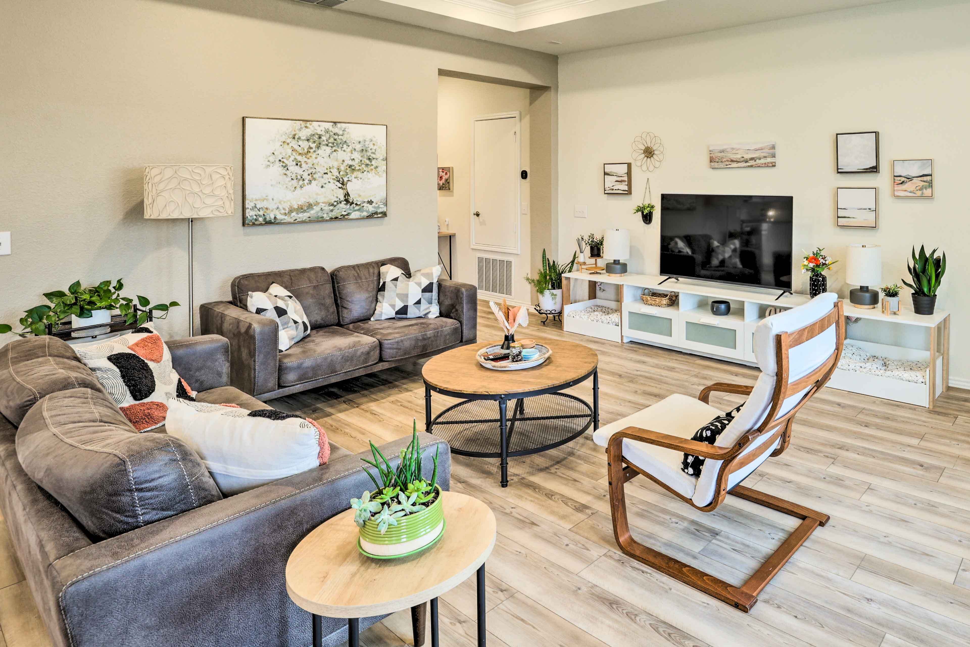 Un salon moderne avec un canapé en cuir, une table basse en bois et une chaise en bois. Un téléviseur à écran plat est posé sur un meuble blanc, et la pièce est décorée dans des tons neutres.