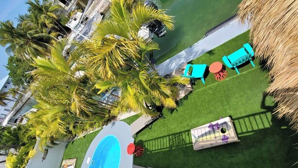 A pool area with artificial grass, a blue pool, and several colorful chairs. - Mad Mahi Canal with pool.<br>This is a pet friendly home. A pet fee and approval of your pet is required. (Summerland Key)