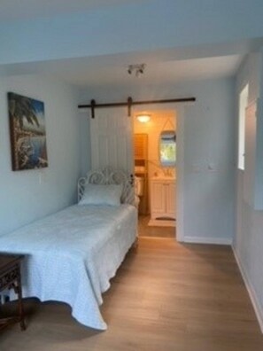 Cozy retreat with a single bed, painting, and access to a bathroom with a mirror and window.