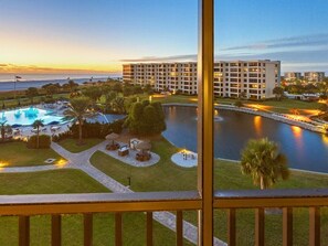 A hotel with a pool, a water feature, and a view of the ocean at sunset.