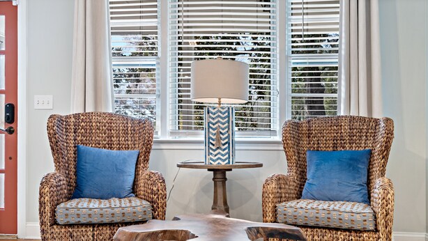 Deux fauteuils en osier avec des coussins bleus, une table basse en bois et une lampe dont le pied est orné d’un motif en chevrons.