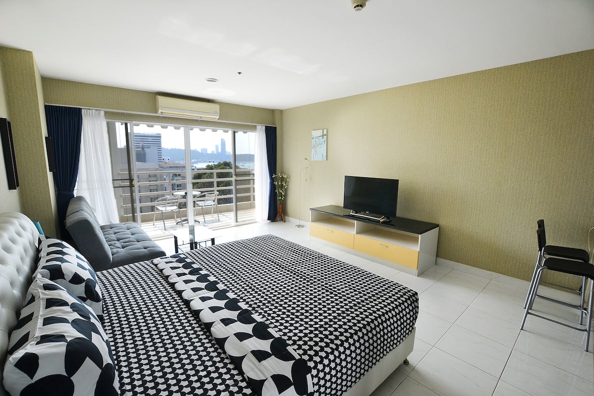 Ein Hotelzimmer mit einem großen Bett, einem Fernseher, einem Balkon und Blick auf die Stadt.