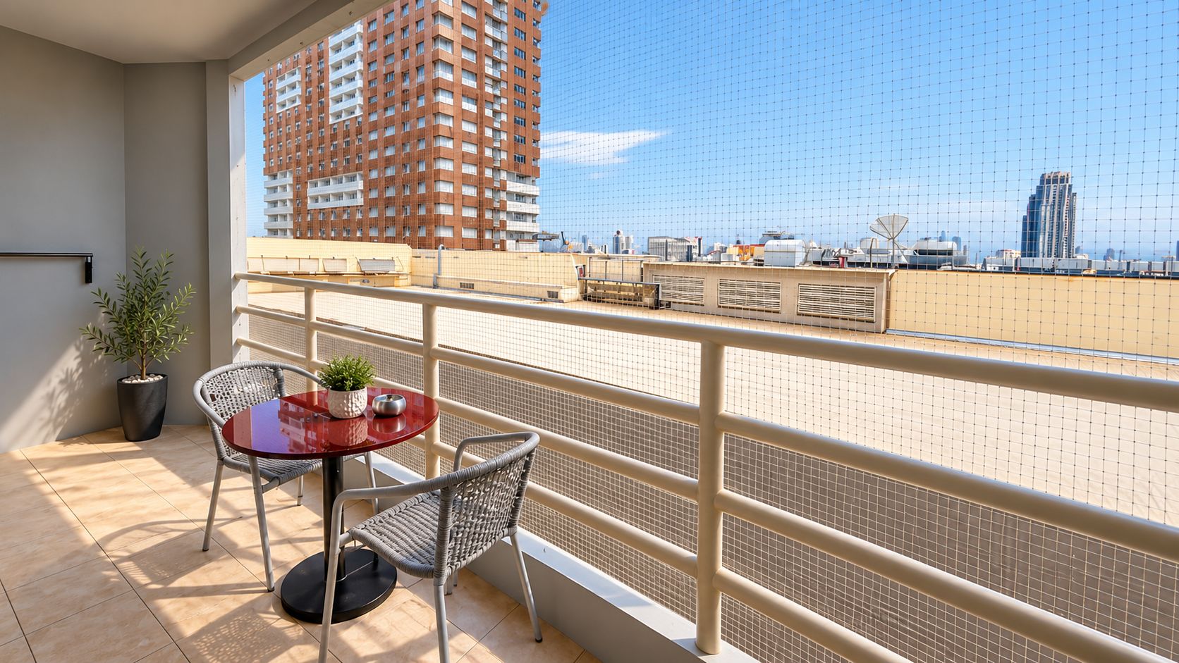 Ein Balkon mit Tisch und Stühlen, einem Blumentopf und Blick auf eine Skyline mit Hochhäusern.