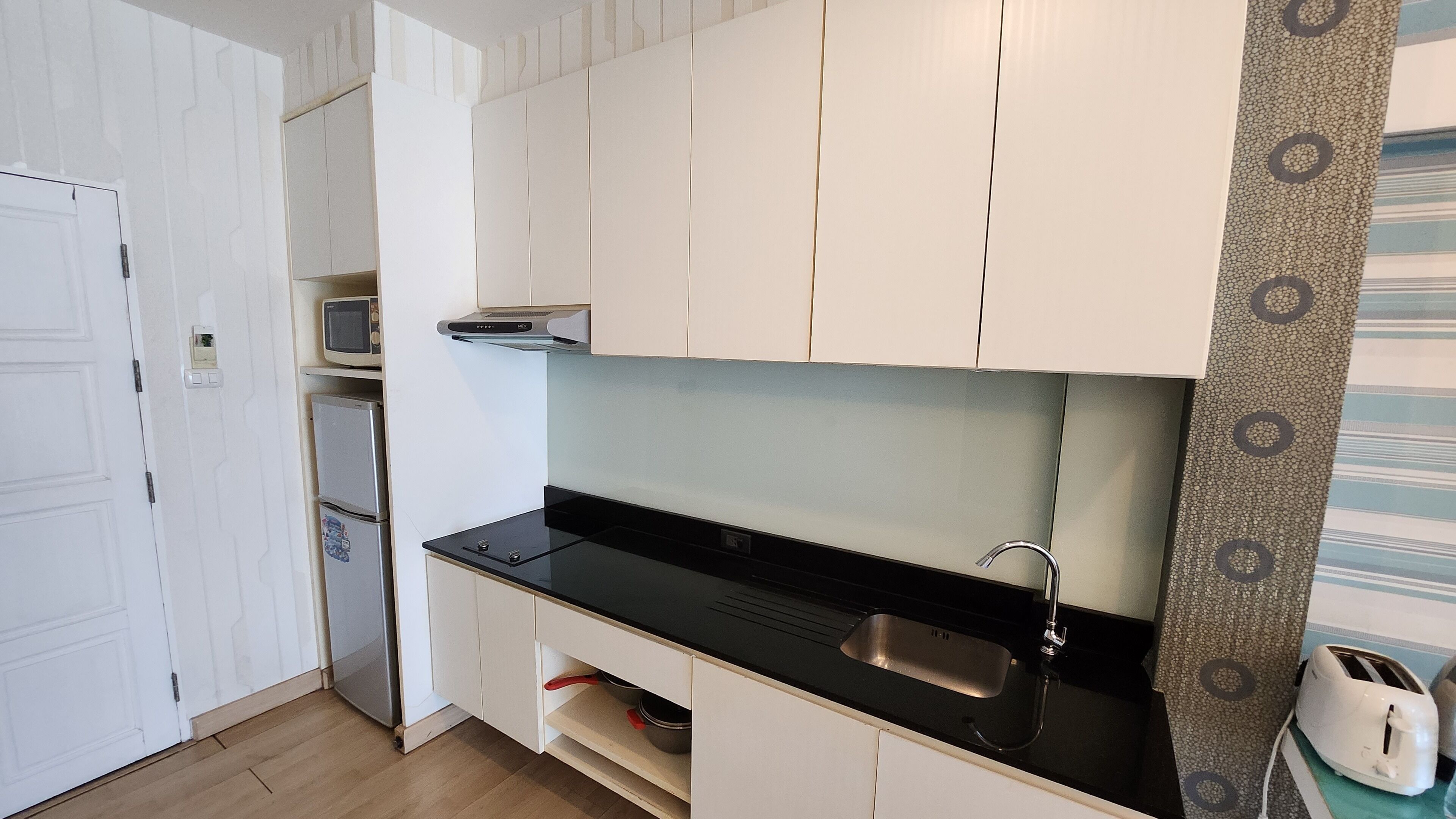 A compact kitchen with white cabinets, a black countertop, a built-in microwave, and a toaster.