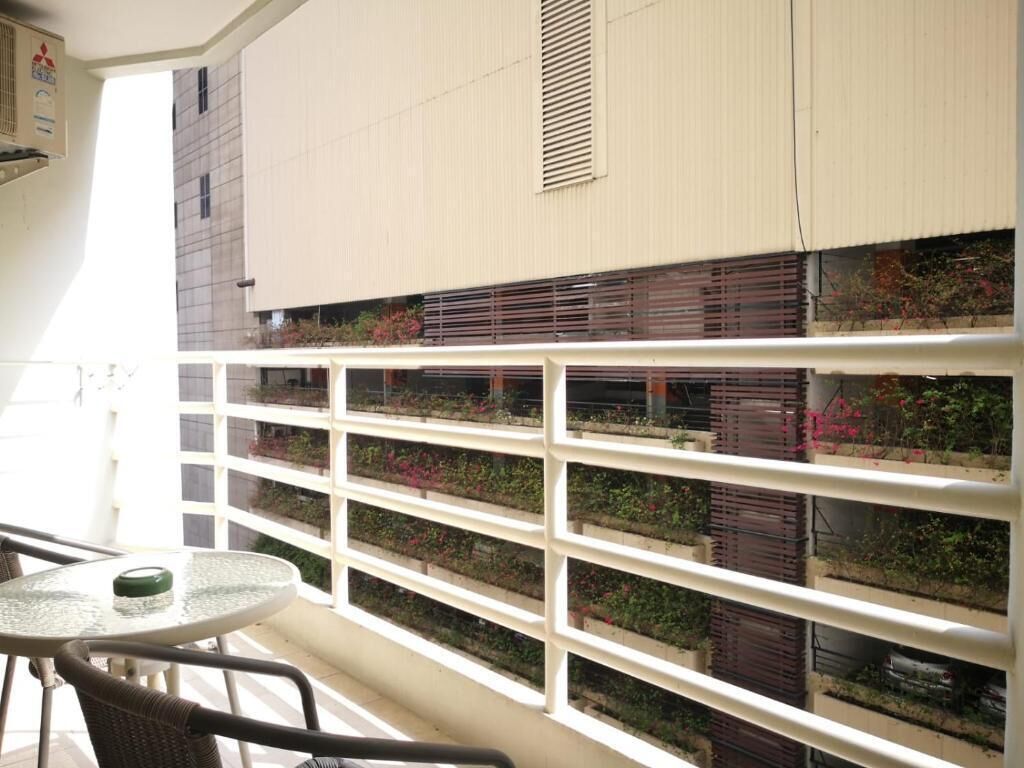 A balcony with a white railing, a glass table, and wicker chairs.